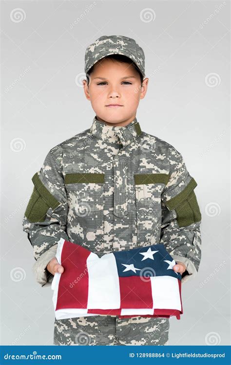 Portrait Of Kid In Military Uniform Holding Folded American Flag Stock
