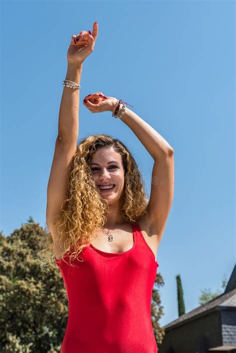 Blonde Girl With Curly Hair And A Red Swimsuit Gesticulating With Her Hand Raised In The Middle