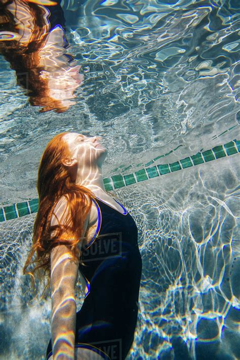 Teenage Girl With Red Hair Swimming Underwater In Pool Stock Photo