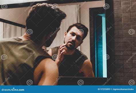 Reflection Of Young Man In Bathroom Mirror Looking On His Face Stock