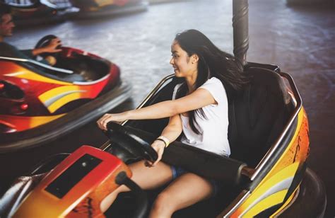 A Woman Is Sitting In A Bumper Car At An Amusement Park While Another Rides Behind Her