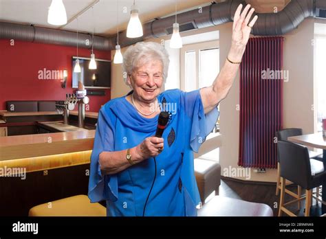 80 year old woman sings karaoke in a bar bar stools and counters in the background she creates