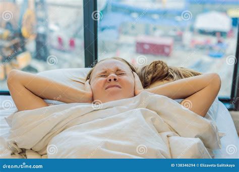 Young Woman Lying On A Bed Covered Her Ears Because Of The Noise In
