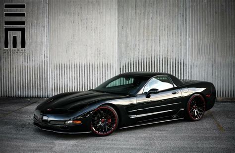 A Black Sports Car Parked In Front Of A Building With Red Rims On It