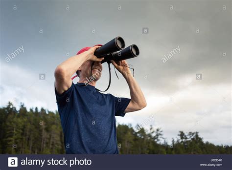 Senior Man Looking Through Binoculars Toward Coast Of Maine Usa Stock