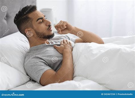 Sick Young Arab Man Coughing While Lying In Bed At Home Stock Photo
