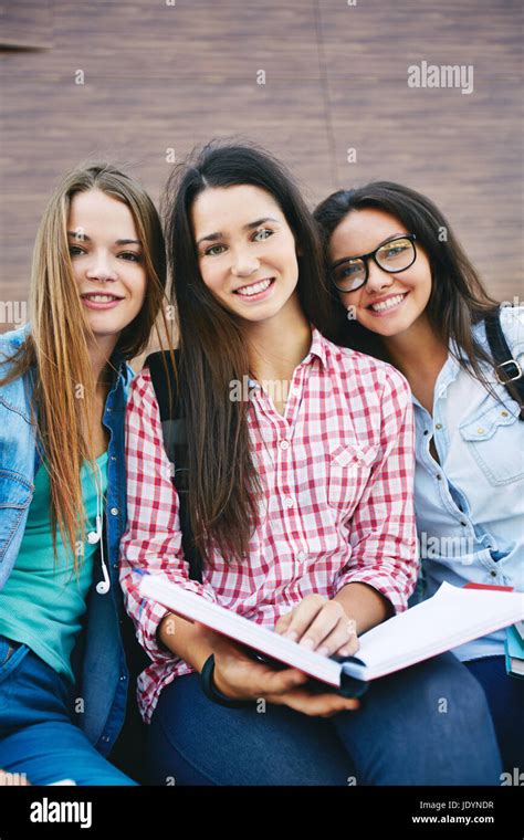 Company Of Happy Teen Girls With Open Book Looking At Camera Outside