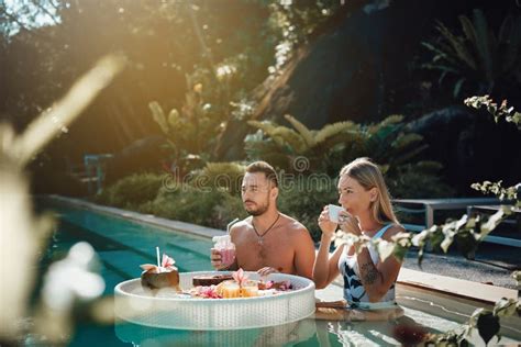 Joyful Husband And Wife Swim In Pool Together Drinking Cocktails Stock