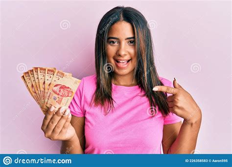 Young Latin Girl Holding Mexican Pesos Smiling Happy Pointing With Hand