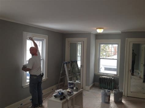 A Man Standing In Front Of A Window Painting The Walls And Trimming The