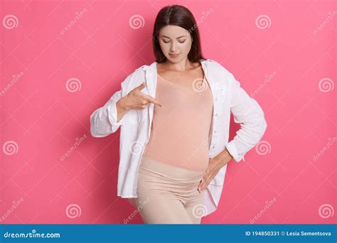 Happy Pregnant Woman Pointing At Her Belly Dark Haired Expectant Mother Looking At Her Stomach