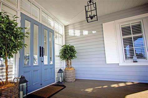 A Blue Front Door With Two Potted Plants On The Porch And A Lantern