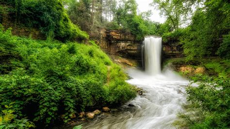 Landscape View Of Waterfall From Rock River Stream Between Green Trees