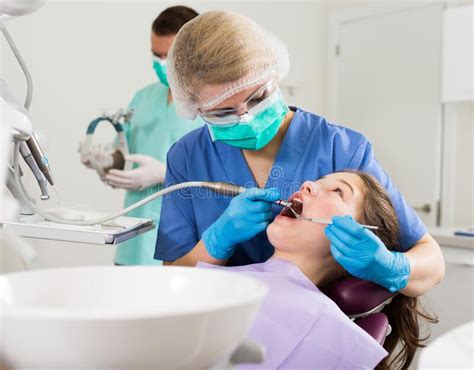 Female Dentist Treating Girl Patient With Male Assistant Stock Photo