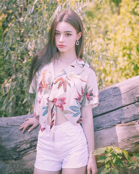A Woman Standing Next To A Wooden Fence Wearing White Shorts And A Floral Shirt With An Open Back