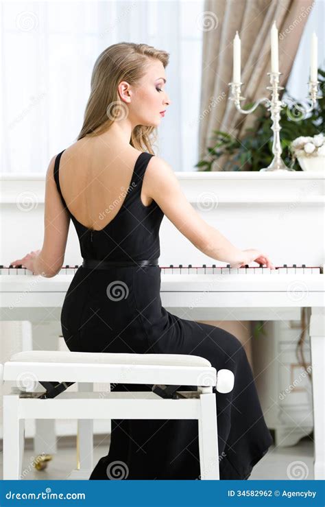Back View Of Female Pianist Sitting And Playing Piano Stock Photo
