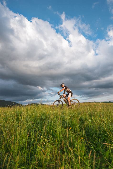 Cyclist Man Riding A Bicycle In Green Field Near A Thunderstorm By Stocksy Contributor Ibex