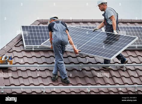 Men technicians carrying photovoltaic solar moduls on roof of house