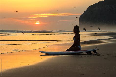 Woman Sitting On The Sunset Beach With Surfboard By Stocksy