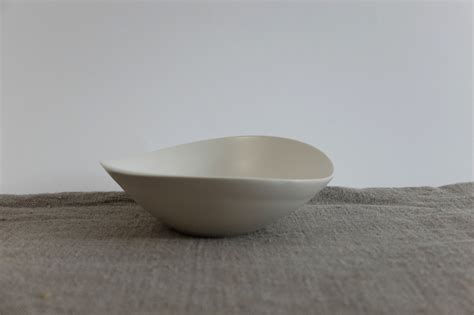 A White Bowl Sitting On Top Of A Gray Cloth Covered Table Next To A Wall