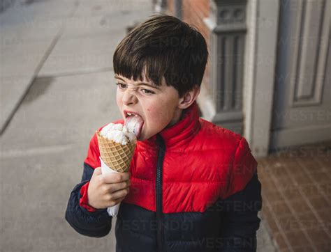 Boy Looking Away While Licking Ice Cream On Footpath In City Stock Photo