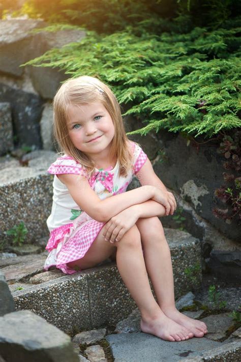 Mała Dziewczynka W Sukience Siedzi Na Kamiennych Schodach W Ogrodzie Goły Uśmiech Stóp Zdjęcie