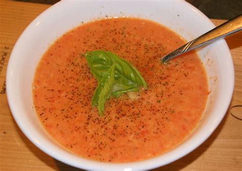 a white bowl filled with tomato soup and garnished with basil leaves on top