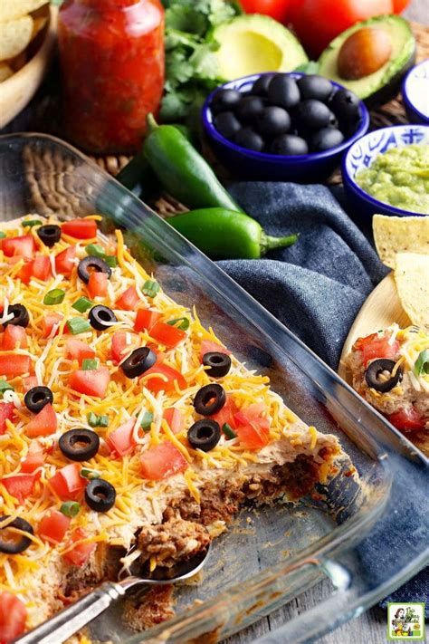 A Casserole Dish Of Taco Dip With Cheese Olives Tomatoes And Green