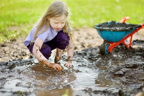 Funny Little Girl Playing In A Large Wet Mud Puddle On Sunny Summer Day