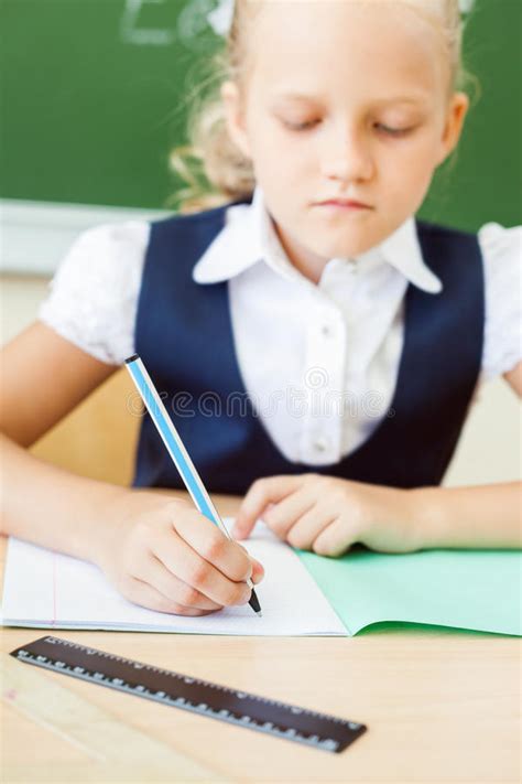 Schoolgirl Sitting At Desk At School And Writing To Notebook Stock