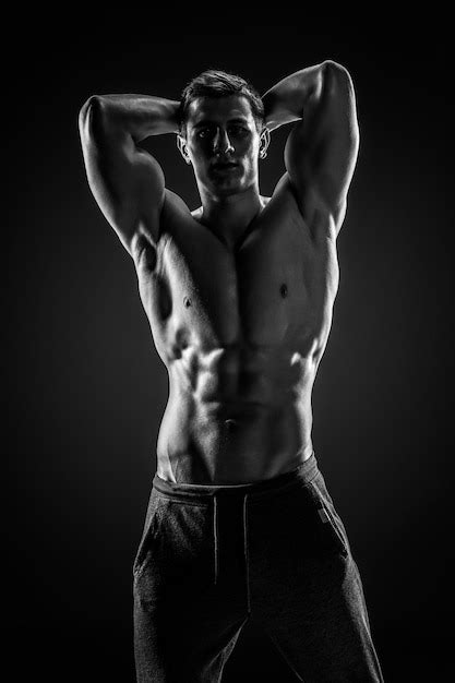 Sexy bodybuilder mit nacktem oberkörper posiert blick in kamera auf schwarzem ba Premium Foto