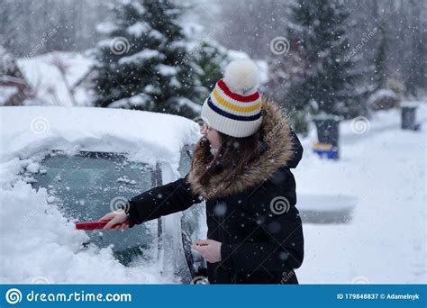 Young Attractive Brunette Woman Clearing Snow Off A Car With A Ice