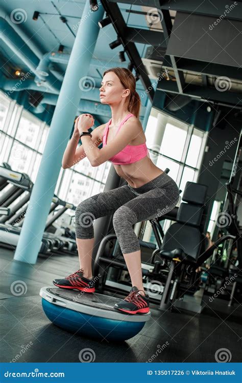 Young Girl In Gym Healthy Lifestyle Standing On Bosu Trainer Squatting