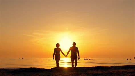 A Man And A Woman Go To The Sea At Sunset Holding Hands Silhouettes