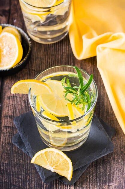 Premium Photo Pieces Of Lemon In A Glass Of Water And Rosemary On A
