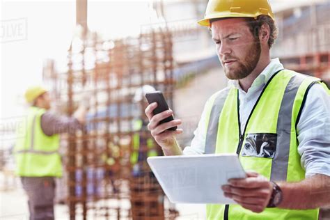 Construction Worker With Digital Tablet Texting With Cell Phone At