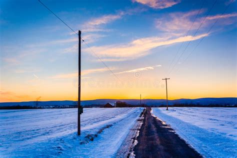 Sunset Over A Country Road Through Snow Covered Fields In