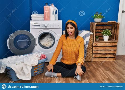 Young Hispanic Woman Doing Laundry Sticking Tongue Out Happy With Funny