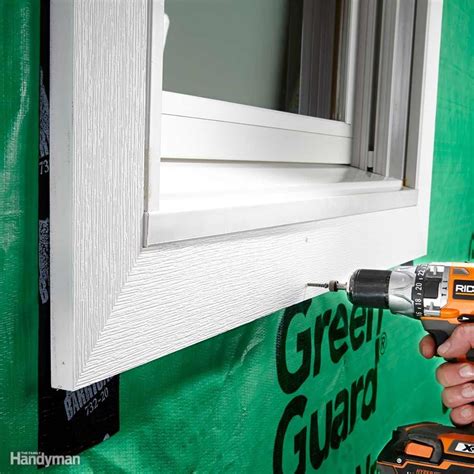 A Man Is Holding A Drill And Drilling The Window With A Green Guard