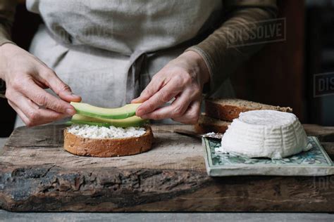 Woman Placing Slices Of Avocado Onto Sliced Bread With Ricotta Mid Section Stock Photo Dissolve