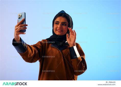 بورتريه لإمرأة عربية خليجية سعودية، تحمل بيدها الهاتف المحمول إجراء مكالمة فيديو، تصوير سلفي