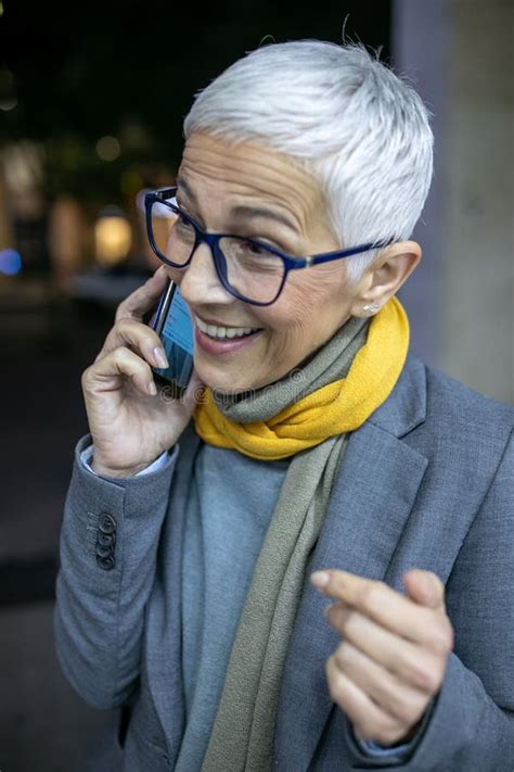 Smiling Mature Senior Woman With Short Gray Hair And Eyeglasses Use Phone On Street Night Scene