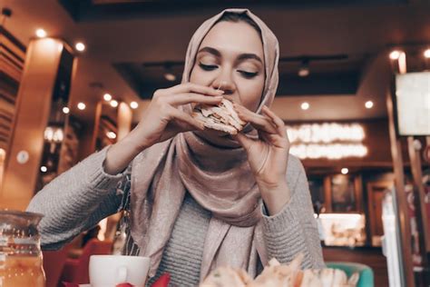 Premium Photo Hungry Young Arab Girl In Hijab Eating Tasty Food In A