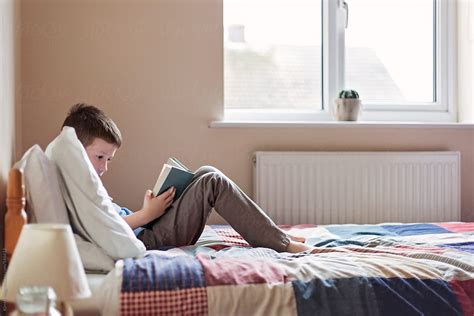Boy Reading A Book While Lying On A Bed By Stocksy Contributor