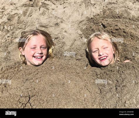Portrait Of Smiling Girls Buried In Sand Stock Photo Alamy
