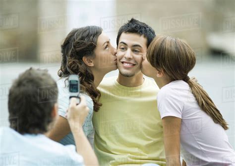 Teen Girls Kissing Boys Cheeks While Second Boy Takes Photo Stock