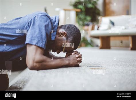 African American Male Praying On His Knees With His Head Down At The