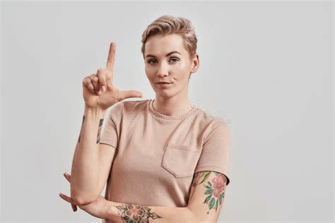 Portrait Of Confident Tattooed Woman With Pierced Nose And Short Hair In Beige T Shirt Holding