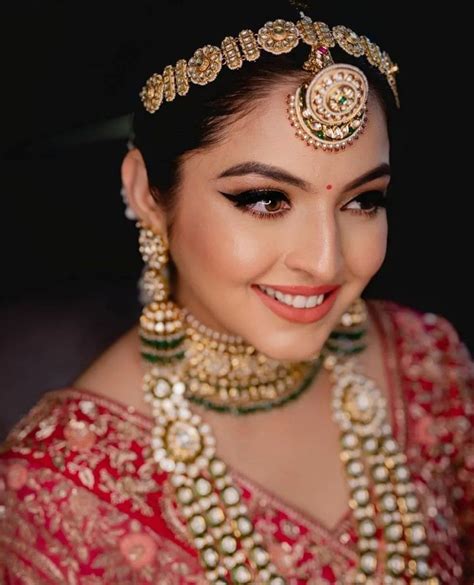 a woman in a red and gold bridal outfit with jewelry on her head smiling at the camera