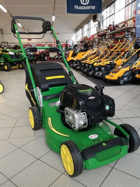 A Green Lawn Mower Sitting On Top Of A Tile Floor Next To Rows Of Tractors